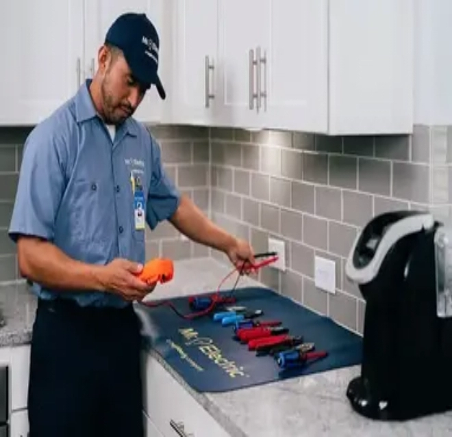 A Mr. Electric Electrician Stands at a Counter with Tools Spread Out on it and Uses a Device to Test an Electrical Outlet