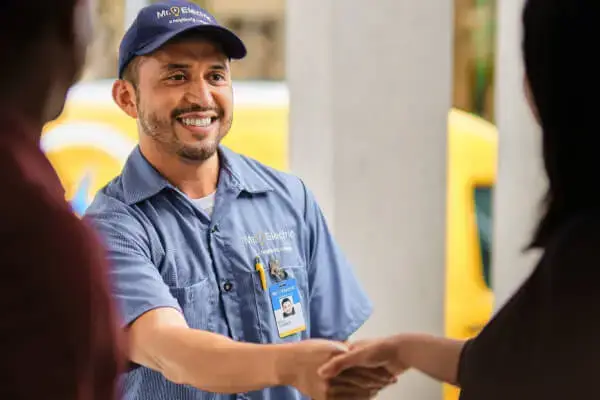 A smiling Mr. Electric electrician shakes hands with a woman at the doorway.