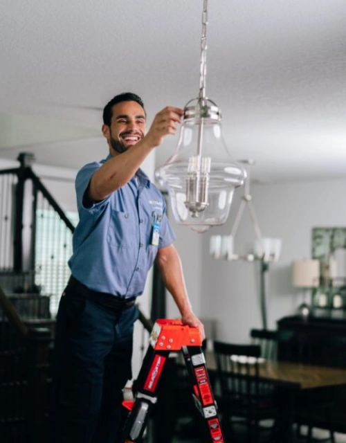 Electrician standing on ladder, adjusting a light fixture.