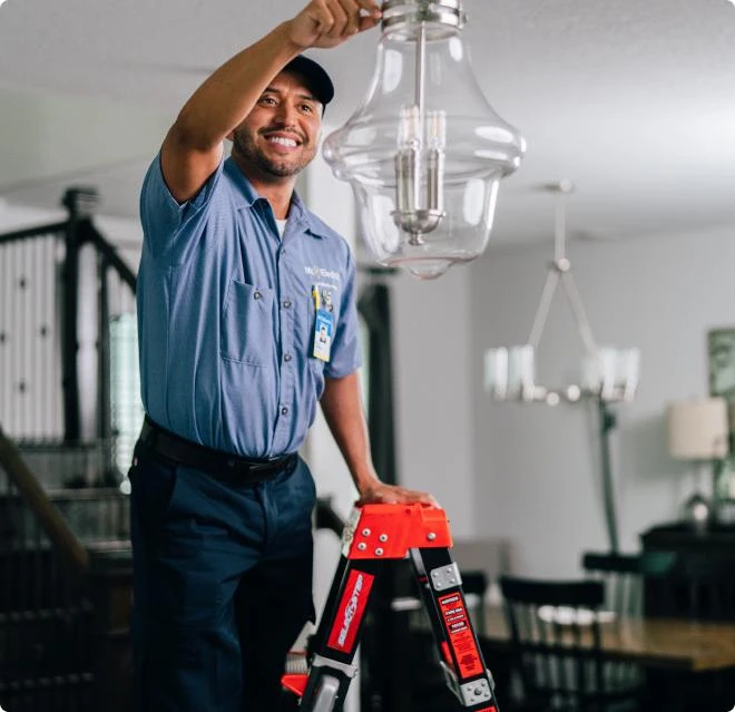 Mr. Electric electrician is on a ladder adjusting a ceiling lamp.