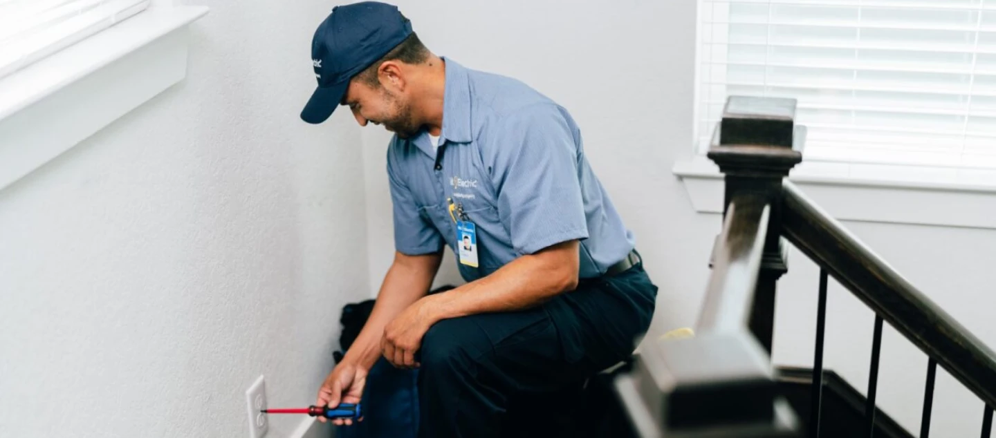 A Mr. Electric electrician kneeling down to install an electrical outlet in a home stairwell