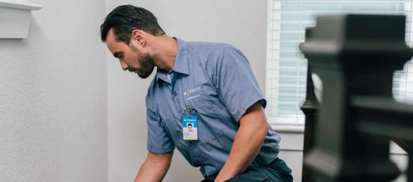 Electrician kneeling to fix outlet.