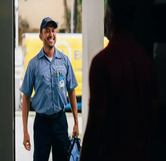 A Mr. Electric electrician in front of a door holding a bag looking at a man inside the doorway.