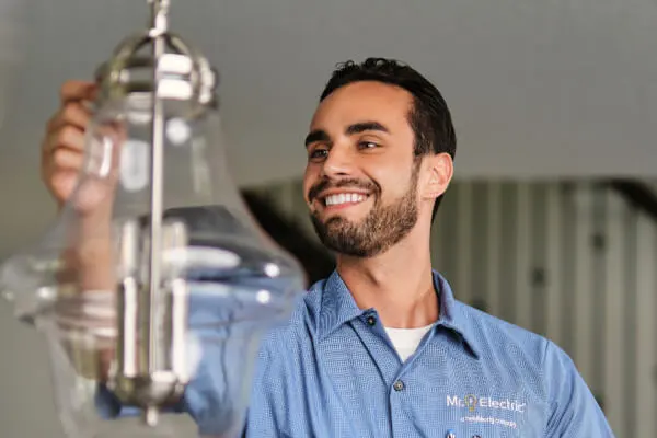  A Smiling Mr. Electric Service Professional Reaches Out to a Pendant Light Fixture Suspended from a Ceiling