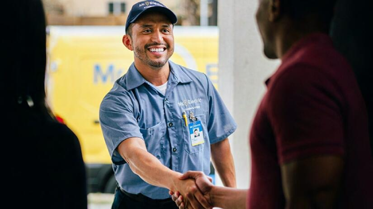 A Mr. Electric Employee Wearing a Blue Button-Down Uniform Knocking on a White Home Door