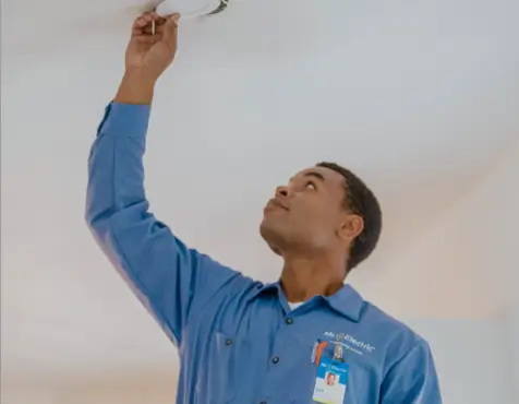 Electrician in blue uniform reaching up to install or check a ceiling light fixture, 