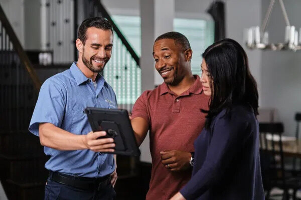 A Smiling Mr. Electric Electrician Shows a Tablet to a Man and Woman Standing Next to Him.  