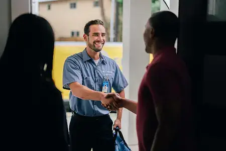 Mr. Electric technician smiling outside of the front door while shaking the hand of the homeowner.