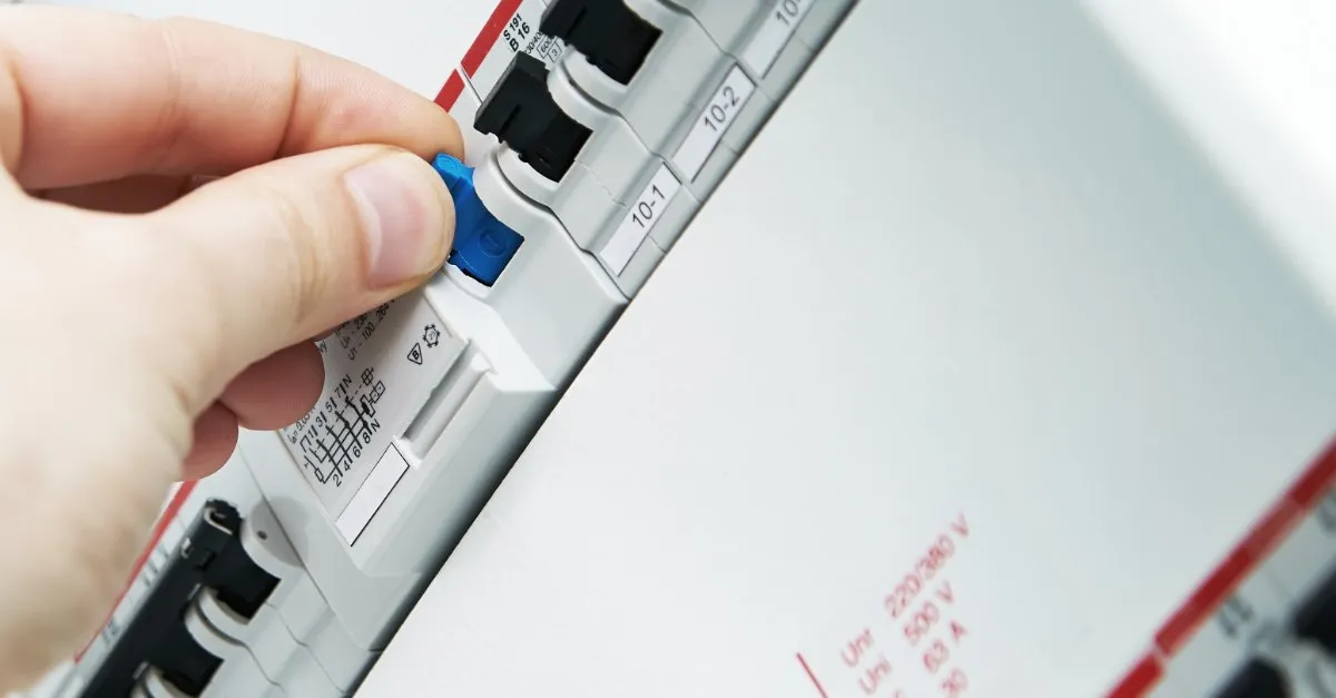 A close-up of a circuit breaker in Colorado Springs with one circuit tripped and a hand poised to switch it back on.