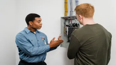 Professional electrician examining residential circuit box with a homeowner.