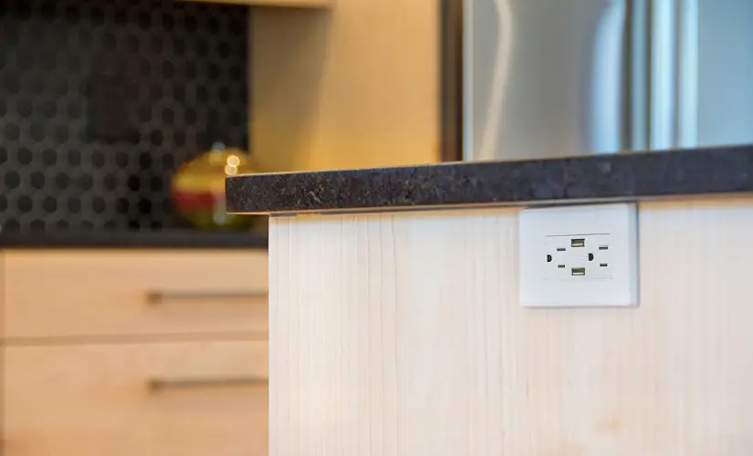 Electrical outlet on the side of the kitchen counter.