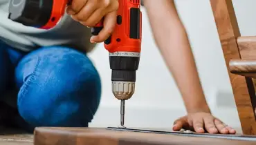 Person using a power drill to attach metal to wood.