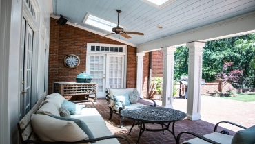 Outdoor patio area of a residential home with furniture, ceiling fan, and white French doors. 