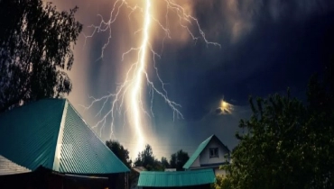 Thunderbolt over the house with dark stormy sky in the background and moon shining through the cloud.