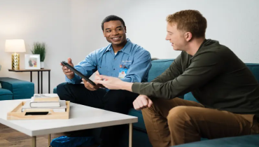 Male service professional and male homeowner sitting in a living room and smiling at a tablet.