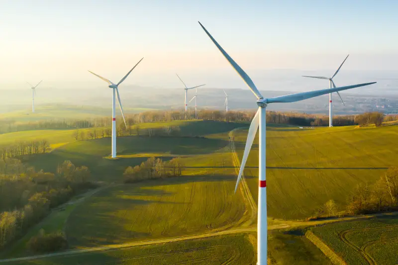 Large windmills standing over a green field with trees.