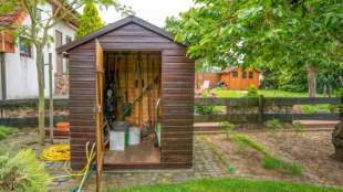 Garden tool shed in backyard of residential home, with door open showing tools neatly arranged inside.