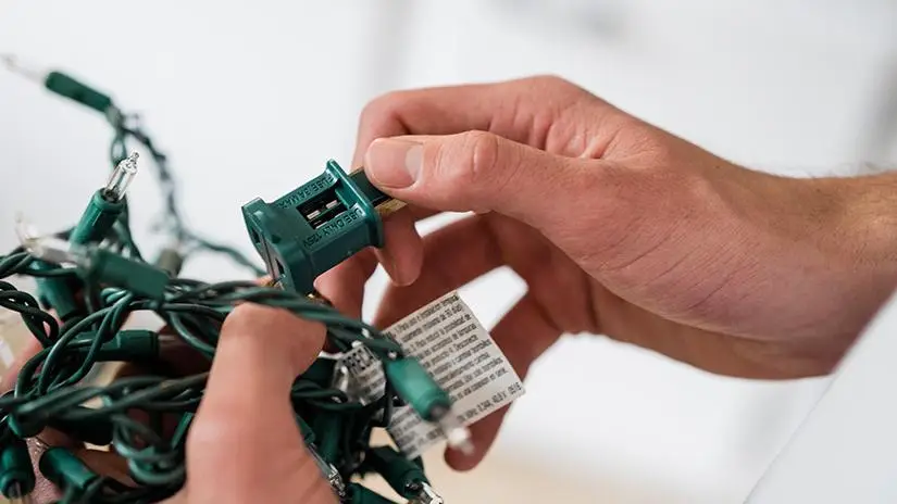 Close-up of hands holding up string of Christmas lights with blown fuse.