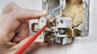 Closeup of a person using a screwdriver to replace a light switch.