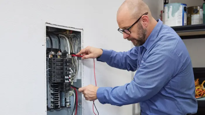 Professional Mr. Electric technician testing a residential electrical panel to ensure home safety during National Electrical Safety Month.