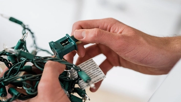 Close-up of hands holding up string of Christmas lights with blown fuse.