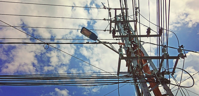 Looking up at utility pole with clouds in the background.