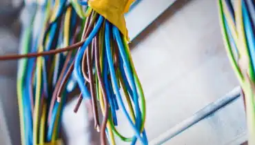 Numerous bundles of multi-colored wires hang down from an electrical installation.