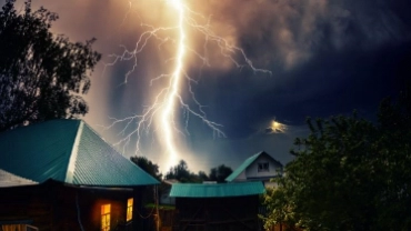 Thunderbolt over the house with dark stormy sky in the background and moon shining through the cloud.