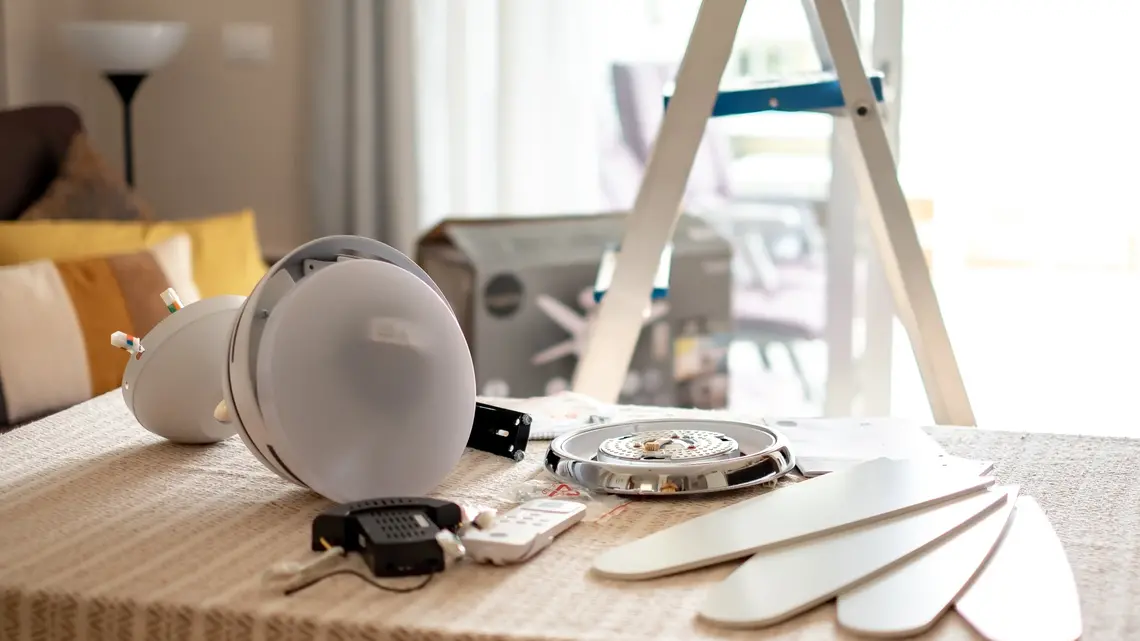 a light kit for a ceiling fan laid out on a table in front of a stepladder.