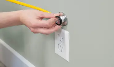 Hand holding stethoscope to wall. 